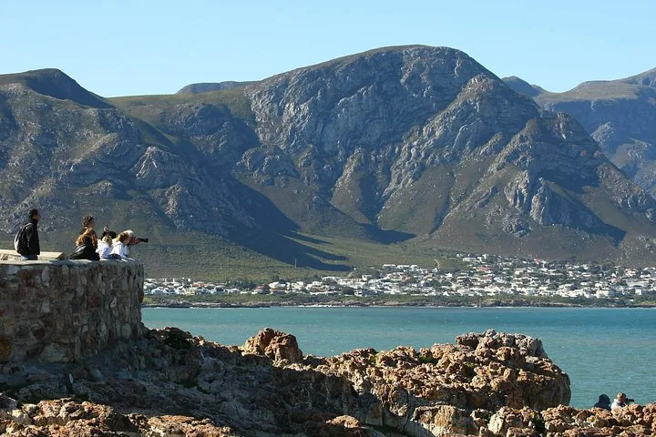 People standing on a stone wall overlooking the ocean and coastal town.